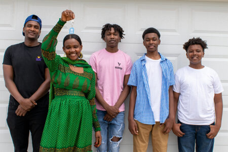 a smiling new Habitat homeowner holds up keys to her new home surrounded by her children