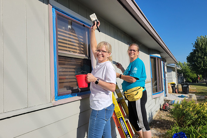 two women smile while painting a neighborhood revitalization house