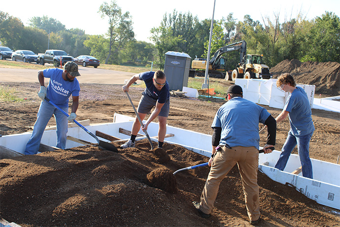 a future Habitat homeowner works with volunteers to even out dirt for a home foundation