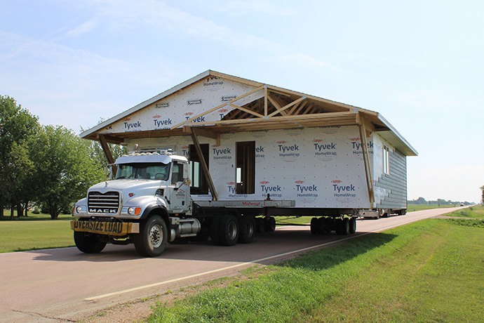 a home built by local students is moved to a Habitat foundation by a large truck