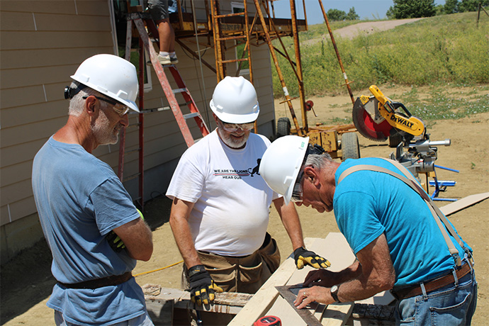 three men in hard hats and safety glasses measure siding on a construction site
