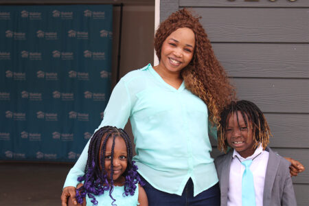 a new homeowner smiles with her two children in front of their new home