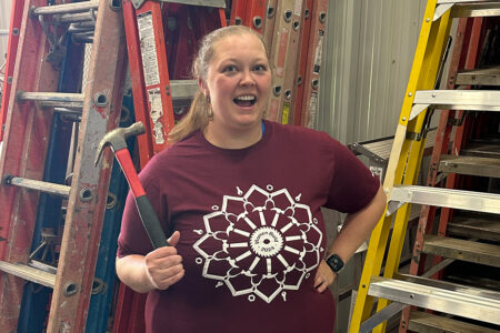 Habitat's Volunteer Coordinator Brittany smiles wearing the Women Build 2024 t-shirt and holding up a hammer