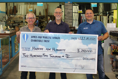 two of James and Marlene Winker's children present a check to Habitat's executive director, Rocky Welker