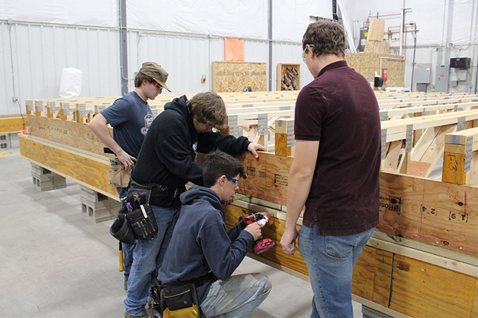 Harrisburg's CTE instructor watches a student as he drills into the framing of the base of the home. One student is measuring to ensure the base is a certain distance from the string line.