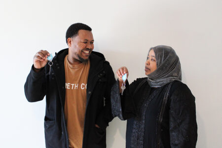 Ali and Rumiya look at each other and smile while holding up the keys to their new home.