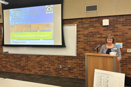 Habitat's homeownership coordinator Lisa stands at a podium ready to present during a previous year's homeownership meeting at the downtown library.