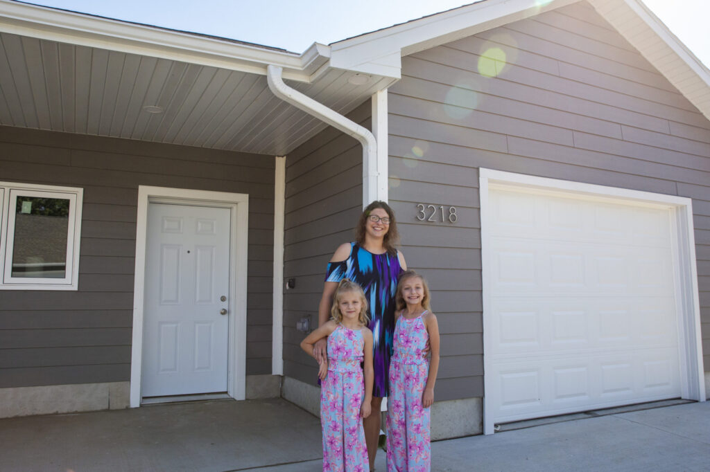 New homeowner Dalonda and her two daughters smile in front of their new home.