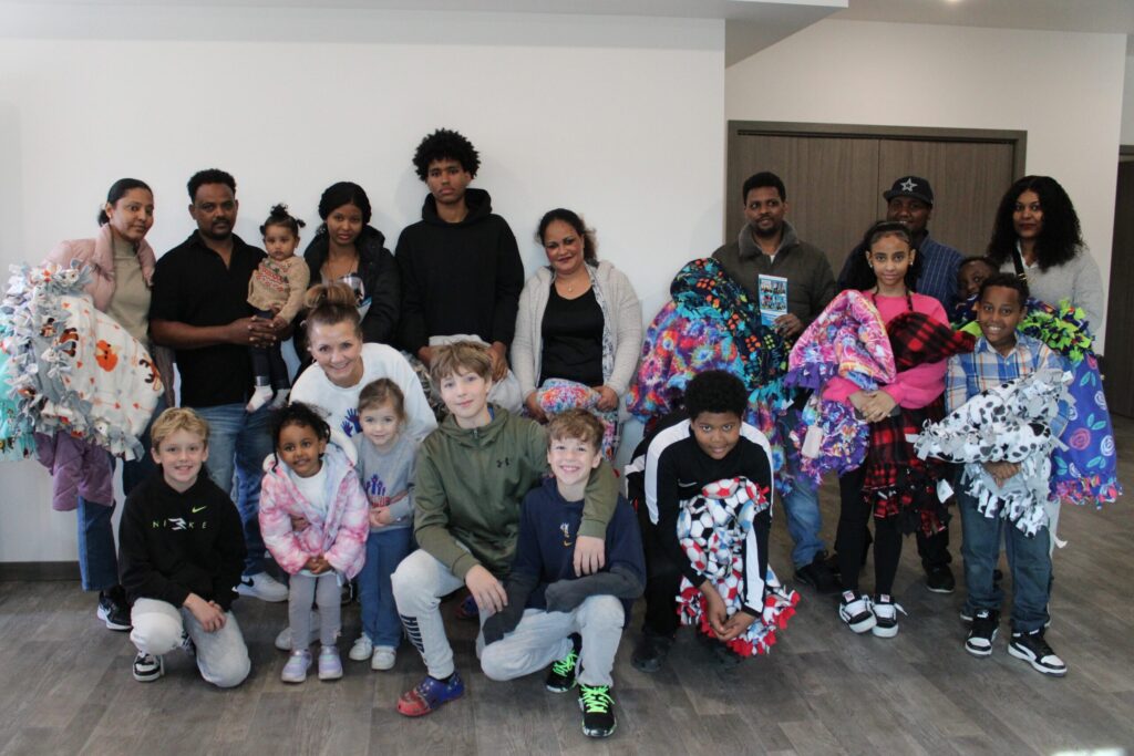 The four new homebuyer families smile with the Project Warm-Up team after receiving blankets at their home dedication.