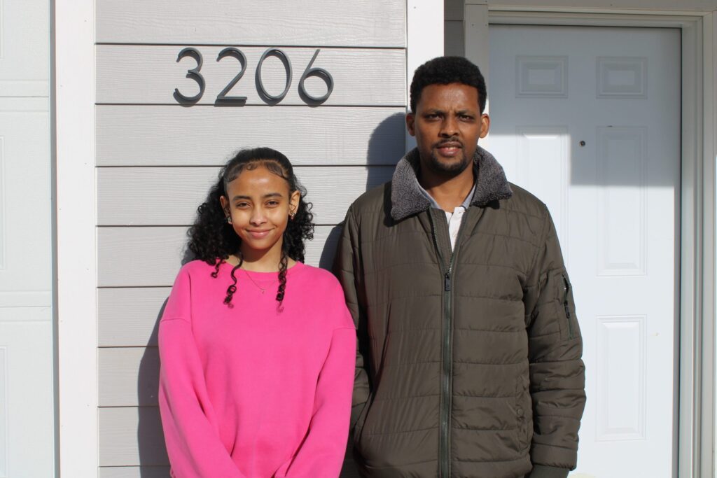 Tesfaye smiles with one of his daughters in front of their new home.