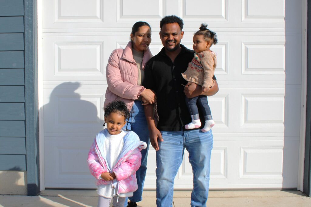 Wegihu and Bisrat smile with two of their daughters in front of their new home.