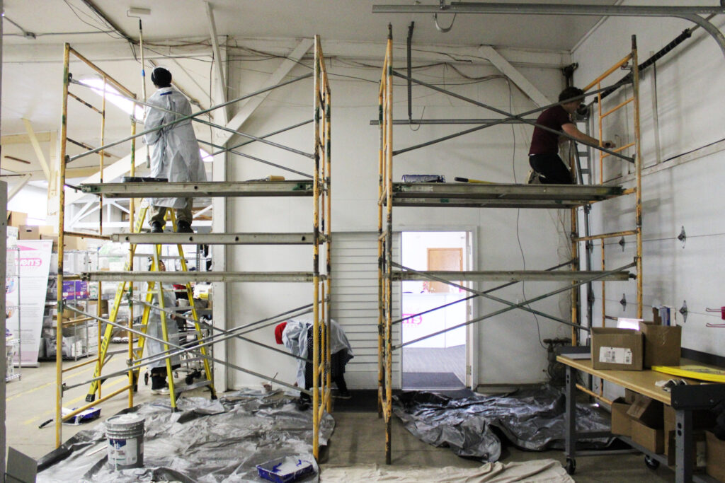 Scaffolding is set up inside the Owen's Outfitters warehouse and Habitat volunteers are on it to paint the warehouse walls and ceiling.