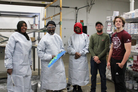 Habitat's NR coordinator and volunteers smile with their painting gear in the Owen's Outfitters warehouse.