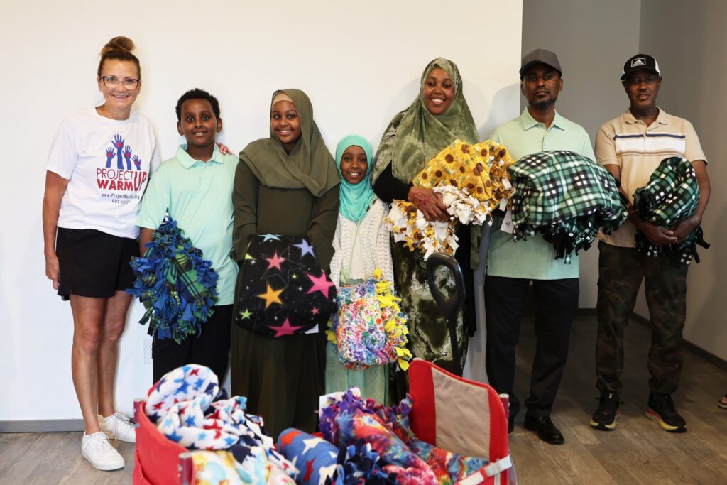 Tracy Vik from Project Warm-Up smiles with the families who hold blankets they received at their home dedication.