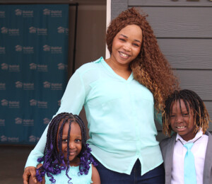 a new homeowner smiles with her two children in front of their new home
