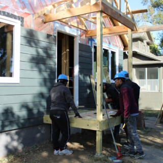 Volunteers work to nail in floor boards for the new front porch. The gable is framed but not yet sided or shingled.