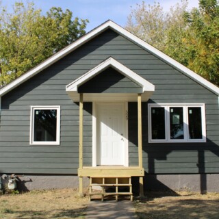 With a little more work, we were able to finish up the home's exterior in October. This winter, we'll continue working on the interior of the home. Thanks to everyone who has helped us make so much progress on this rehab house! The front of the house. There are new windows, new grey siding and a finished front porch and stairs covered by a gable.