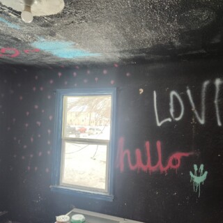 Walls were covered in spray painted graffiti, and light bulbs were exposed. A room painted black is covered in pink, white and teal spray-painted dots, a smiley face and the words "love" and "hello". There is a white circle on the ceiling with an exposed light bulb.