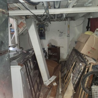A basement is filled with debris. The electrical box does not have a cover, so wires are visible.