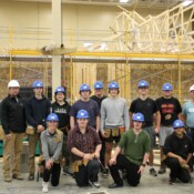 A group of students and instructors from CTE Academy smile in front of their partially constructed Habitat home.