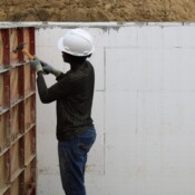 Rebecca, the future homebuyer, works to get the foundation of the home ready. A woman wearing a hardhat and gloves hammers supports for the foundation.