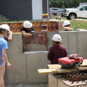 Volunteers work to get the foundation of the home ready. A group of volunteers with hardhats and hammers work on the foundation of the home. They are being instructed by Jolynn, Habitat's construction site supervisor.