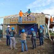 Volunteers work with the Habitat construction team to add a garage to the home. Group of volunteers receive instruction from Dustin, Habitat's volunteer coordinator. The studs and trusses are set but unfinished.
