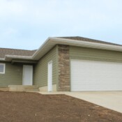 Exterior photo of a home. It's green with white doors and trim. The garage has brick details on both sides of the door.