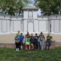 The bandshell is a very light gray with blue/green trim. Volunteers smile and show off their work.
