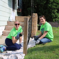 This porch gets a fresh coat of paint, too! Two volunteers smile while holding paint brushes next to the porch railing they're painting.