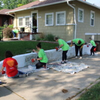 Volunteers are spread out to paint a small retaining wall white.