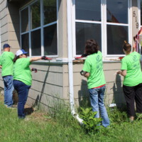 Volunteers use brushes to scrape off old paint from window trim.