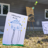 Drawing of a house with "Welcome Home" staked in the yard in front of the twin home.