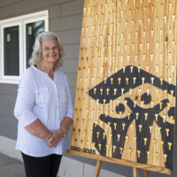 Habitat's first homebuyer Linda stands next to the commemorative 200th home key sign.