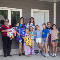 The new homeowners stand holding blankets with the Project Warm-Up team.