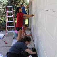 It wouldn't be Rock the Block without a painting project! We were excited to brighten up this garage door with a fresh coat of paint. Volunteers paint a garage door with brushes and rollers.