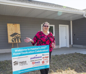 Vickie smiles next to the 200th Home Dedication Celebration sign on her dedication day.