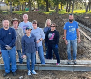 A volunteer group smiles standing in the partially built foundation of a Millard Acre twin home.