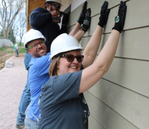 Habitat team members hold siding in place while another team member drills it into the ICF block.