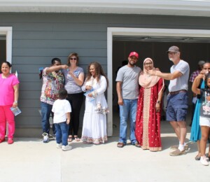 The four 2024 Millard Acres families smile while holding up keys to their new homes along with the supporters who helped make it possible.
