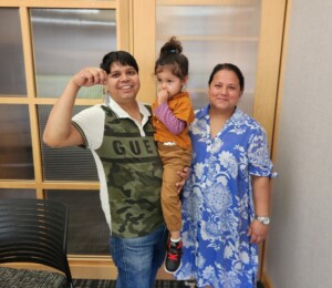 Shyam, Yasodha and their daughter smile at the title company while Shyam holds up their house key.