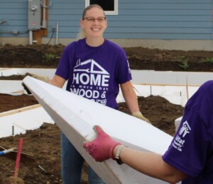 A volunteer smiles while carrying a foundation ICF block during Women Build 2023 in Millard Acres.