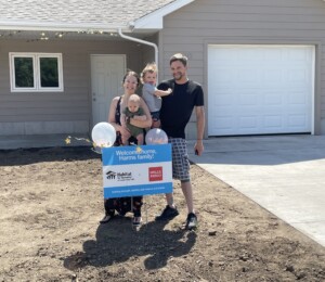 Catie, her husband and children smile in front of their home on their dedication day.