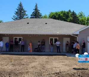Many people stand in a circle on the driveways of Dana and Catie's twin home for their joint home dedication.