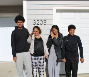 Okuba and her three children smile in front of their new home on dedication day.