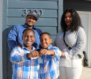 Mitiku, Emebet and their two sons smile in front of their new Millard Acres twin home while the boys hold up a key.