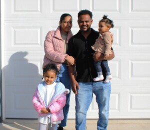 Wegihu, Bisrat and two of their three daughters smile in front of their new Millard Acres twin home on dedication day.
