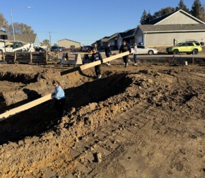 Volunteers carry wood down into the foundation of a Millard Acres twin home.